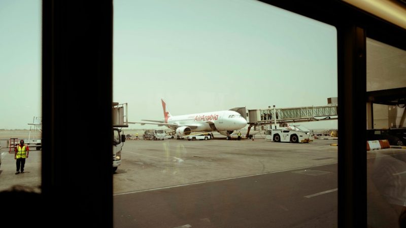 An Air Arabia airplane parked at an airport gate with a jet bridge